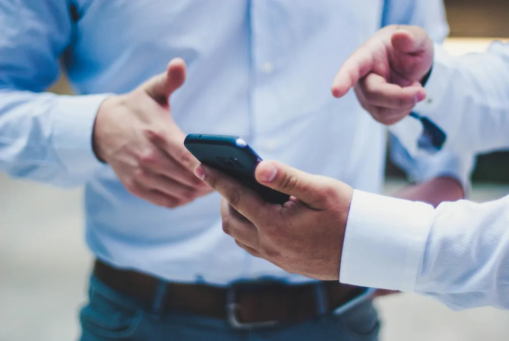 Two people in business shirts talking, one holding a phone.